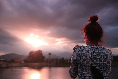 Rear view of woman standing against sky during sunset