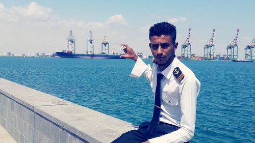 Optical illusion of sailor holding building at harbor by sea against sky