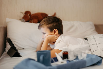 Little boy using tablet while laying in bed in living room. medicines in foreground out of focus