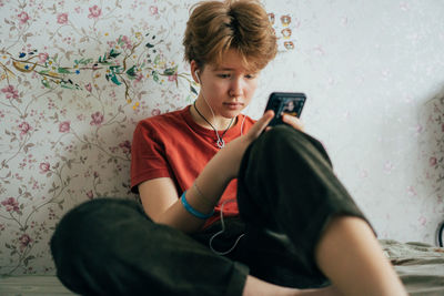 A teenage girl sitting on a bed in a room uses a mobile phone for online communication.