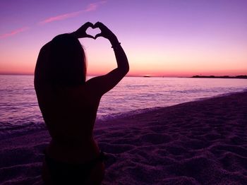 Silhouette woman standing at beach against sky during sunset