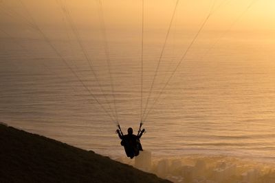 Silhouette man paragliding against sea during sunset