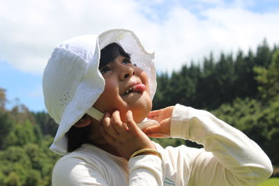 A child with a white summer hat looking up tongue out