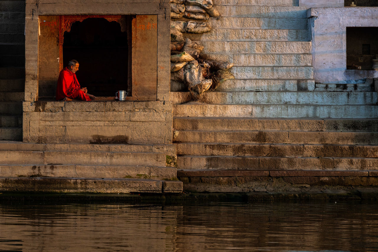 architecture, one person, sitting, built structure, staircase, water, history, real people, relaxation, building exterior, full length, men, the past, day, waterfront, adult, reflection, side view, outdoors