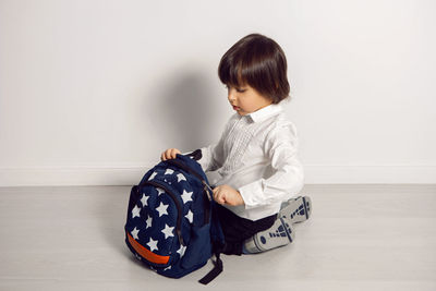 Child boy with a book textbook and backpack sit on a white background