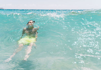 Relaxed white boy with closed eyes diving a wave in the sea in summer