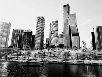 Modern cityscape by river against clear sky