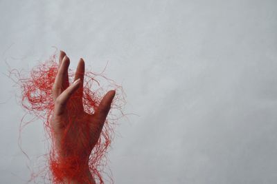 Close-up of woman hand with red tangled strings against wall