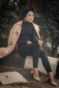 Portrait of young woman sitting on footpath