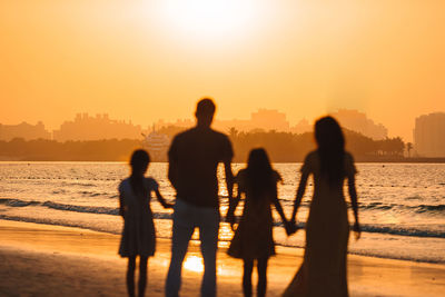 Silhouette people standing by sea against sky during sunset