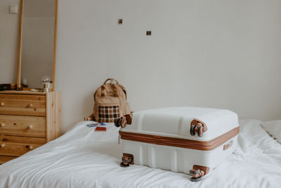 White suitcase and beige backpack on the white bed at home