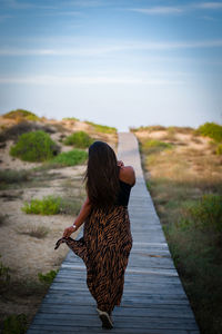 Rear view of woman on footpath against sky