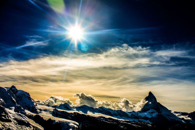 Low angle view of sun shining over snowcapped mountains