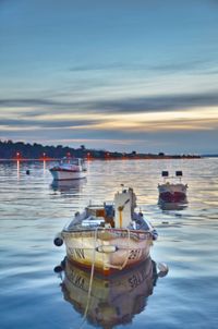 Boats moored in sea against sky at sunset