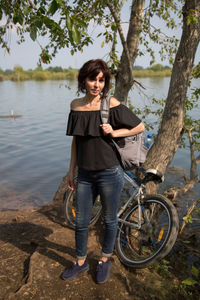 An adult woman with a bicycle stopped shore of a lake enjoying nature.