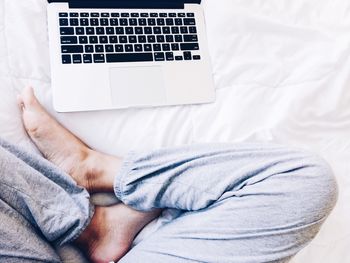 Low section of man using laptop in bed