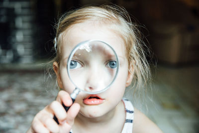 Close-up portrait of girl looking through magnifying glass