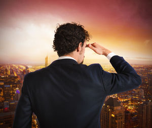 Rear view of man standing by buildings against sky during sunset