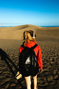 Rear view of woman standing at beach against sky during sunset