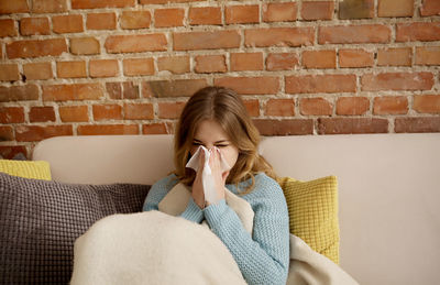 Young woman blowing nose while sitting on sofa at home