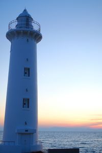 Lighthouse by sea against sky during sunset