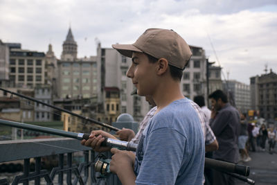 Side view of young man standing against city in background