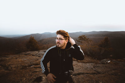 Portrait of young man standing on mountain against sky