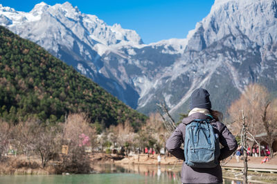 Rear view of woman wearing backpack while standing against mountains during winter