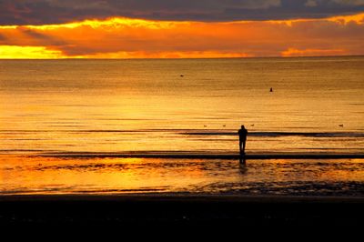 Silhouette person on beach against sky during sunset