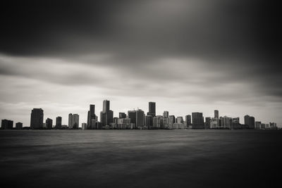 City skyline by sea against cloudy sky