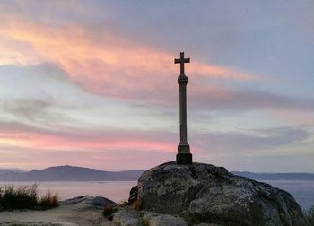 Low angle view of cross sculpture on rock by sea against cloudy sky at dusk
