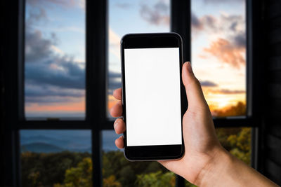 Close-up of hand holding mobile phone against window