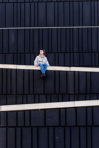 Young teen sitting on a fence while using headphones to listen music