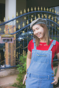 Portrait of smiling woman standing against gate 