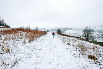 Rear view of girl walking on snow covered landscape