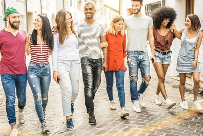 Full length of young friends walking on footpath in city