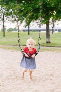 Full length portrait of cute girl leaning on swing over sand