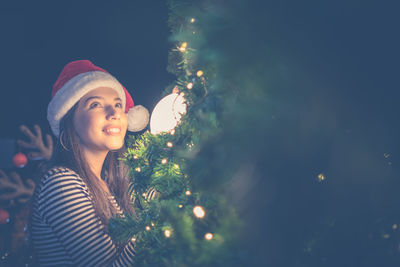 Smiling woman by illuminated christmas tree at night