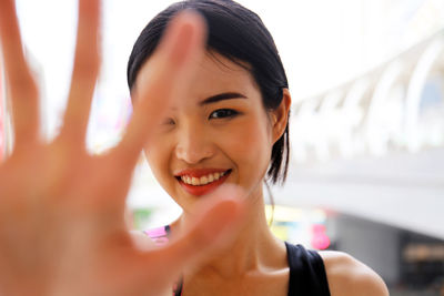 Portrait of smiling young woman gesturing stop sign in city