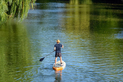 Rear view of man paddling on sup board on river.