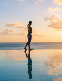 Rear view of woman standing at beach against sky during sunset