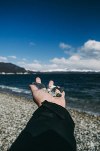 Cropped hand of man holding pebble against sky