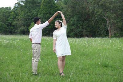 Newlywed couple dancing on grassy field against trees in forest