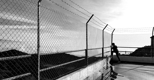 Side view of mid adult man standing by fence against sky