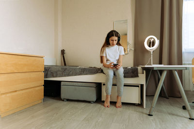 Generation z girl in headphones with a smartphone sits on the bed