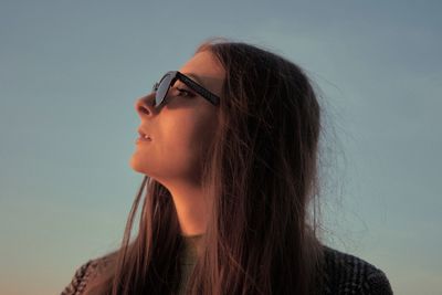 Portrait of young woman looking away against sky