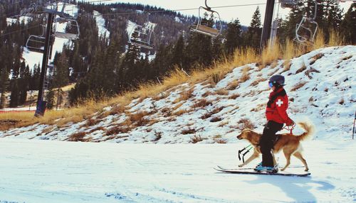 Side view of boy snowboarding with dog on snowcapped field