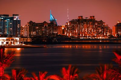 Illuminated buildings by river against sky in city at night