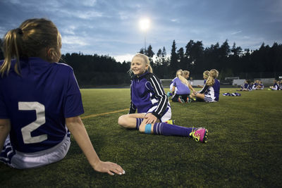 Girls relaxing on soccer field against sky