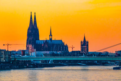 Bridge over river by buildings against sky during sunset